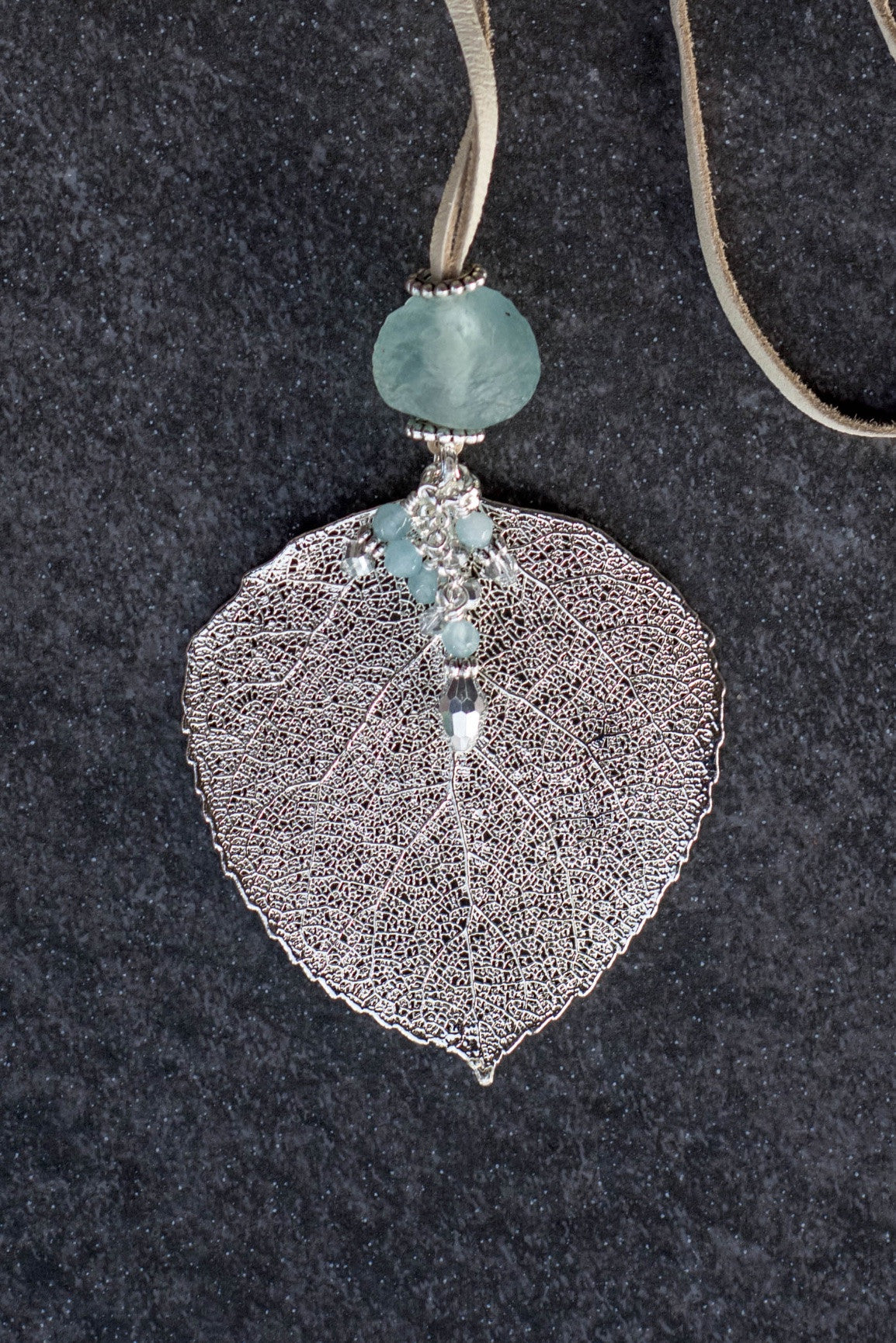 Single re-cycled African glass bead with a large silver Aspen leaf finished with a stunning crystal dangle .  Deerskin leather